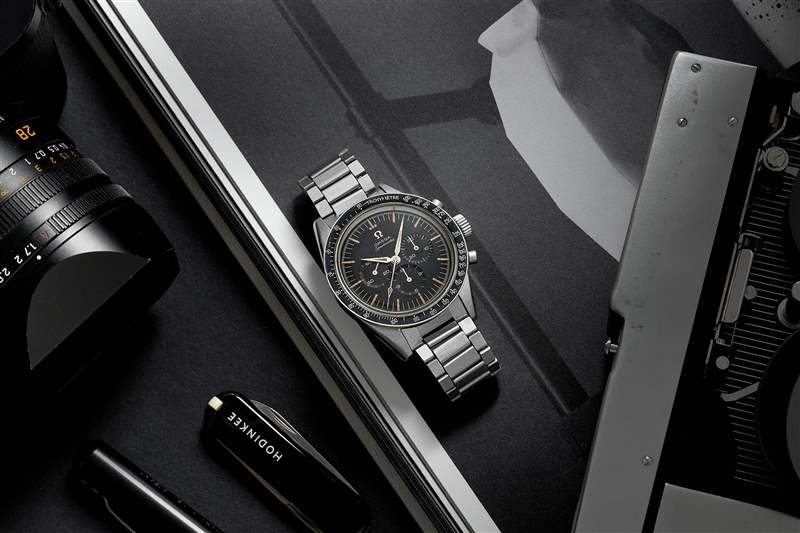 1960 年代 Omega Speedmaster Ref. 的生活方式圖片。 鋼手鏈上的 2998-6 旁邊是一本打開的書、一臺徠卡相機和一把黑色 HODINKEE 品牌的 Victorinox 瑞士軍刀。