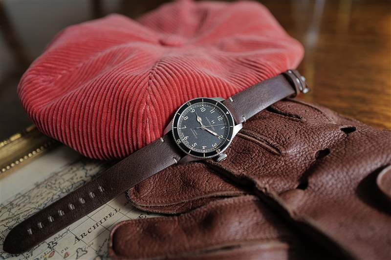 38 毫米尺寸的 Hamilton Khaki Pilot Pioneer 戴紅色帽子，戴著駕駛手套。